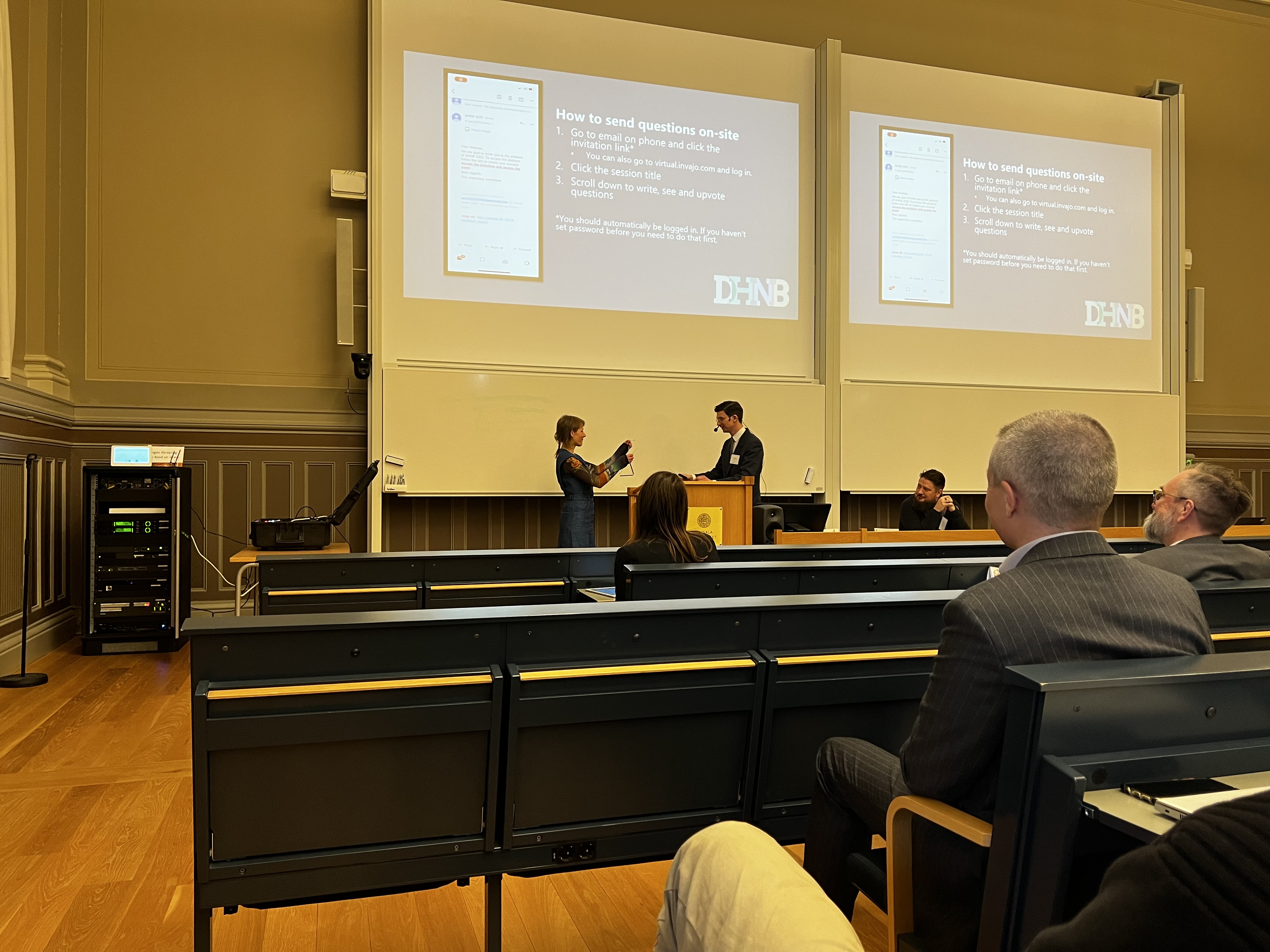 Foto of the opening session of DHNB2022 conference in Uppsala. Anda Baklane hands the triangle over to Karl Berglund.